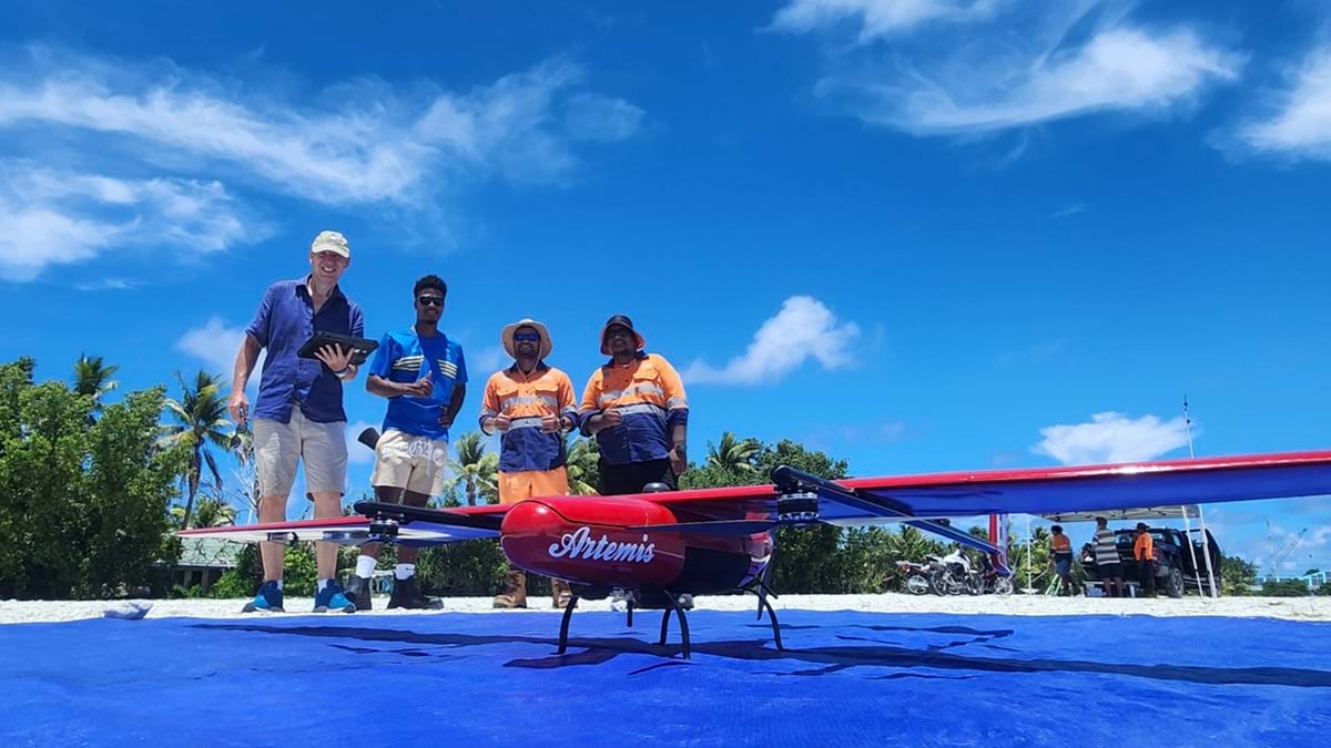 Fixed-wing drone positioned on a launch mat with people standing nearby.