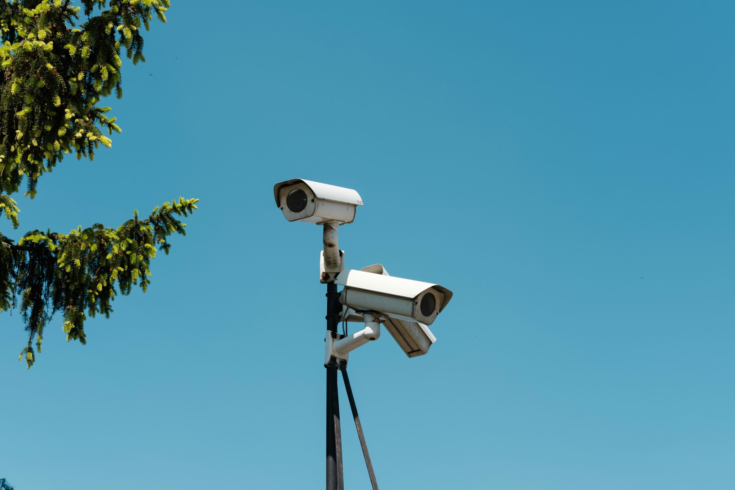 Two surveillance cameras mounted on a pole beneath a blue sky.